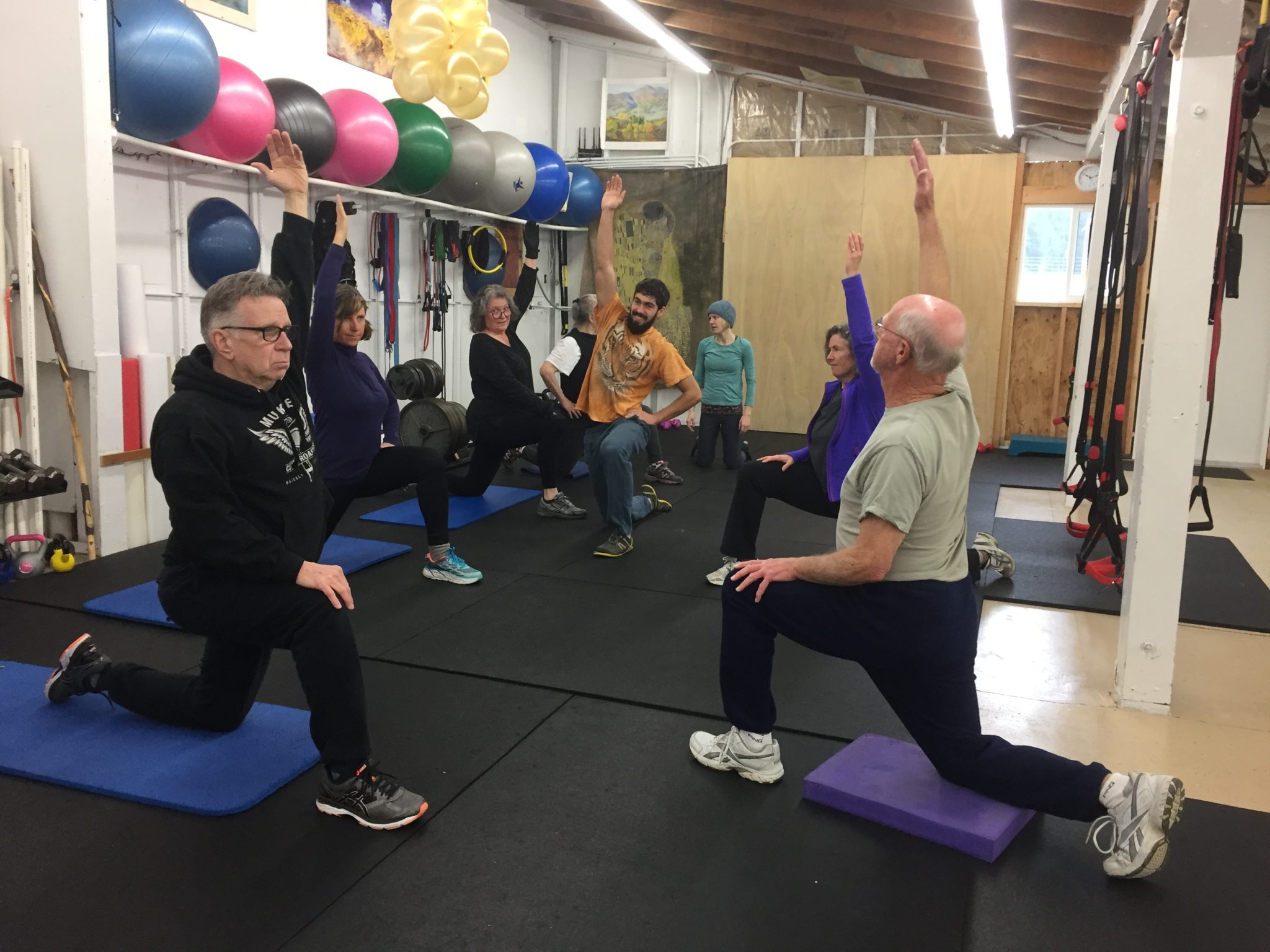 A group photo showing 9 total people doing functional fitness exercises, including Adam Fawcett and adult clients of various ages inside Vibrant Fitness studio together for a photo op. Everyone is smiling happy